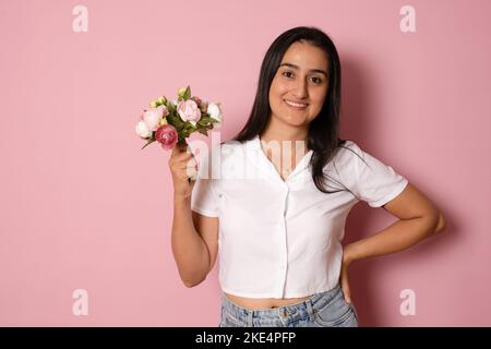 Junge schöne romantische Frau mit langen Haaren hält Blumenstrauß mit einem glücklichen und kühlen Lächeln auf dem Gesicht. Glücklicher Mensch. Stockfoto