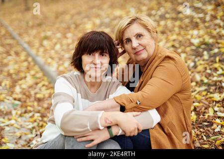 Ältere Rentnerin, Mutter und Erwachsene, fröhliche Tochter, verbringen in der Fallsaison gemeinsam Zeit im Freien im Park. Fröhliche kaukasische Mutter und ihre Tochter sitzen im Herbstpark. Hochwertige Fotos Stockfoto