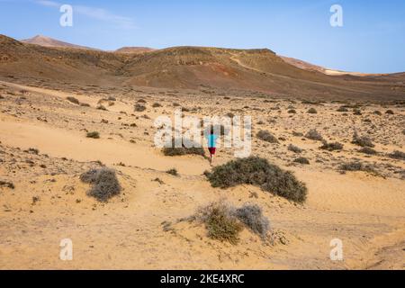 Mann im Urlaub, der einen Spaziergang entlang von Pfaden in vulkanischer Landschaft in der Nähe der Strände von Lanzarote, Kanarische Inseln, Spanien macht. Stockfoto