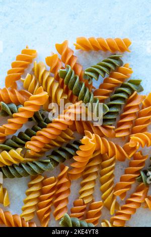 Trockene dreifarbige Fusilli-Nudeln auf weißem Granit-Hintergrund: Stockfoto