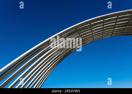 Metallrohre im öffentlichen Raum wölben sich vor dem klaren, tiefblauen Himmel. Stockfoto