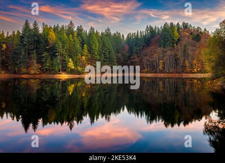 Gespiegelte Farben von Herbstwald und Himmel. Das Foto wurde am 29.. Oktober 2022 auf dem Buhui-See im Kreis Caras-Severin, Rumänien, aufgenommen. Stockfoto