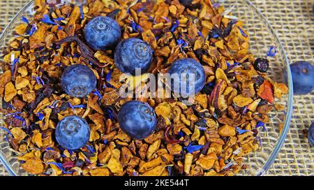 Vollformat Draufsicht Nahaufnahme von isolierten frischen Heidelbeeren auf Pfahlgetrockneten Früchten für die Früchtetee-Zubereitung auf durchsichtiger Glasschale. Jute-Matte-Backgroun Stockfoto