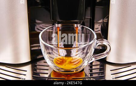 Nahaufnahme des Ausgangs einer modernen vollautomatischen Kaffeemaschine, eine isolierte, transparente Glasbecherfüllung mit frisch gebrühter Café-Crema Stockfoto
