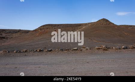 Einsame Wüste in einer trockenen Landschaft in Richtung vulkanischer Berge in der Nähe von Playa Mujeres und der Papagayo-Küste, Lanzarote, Spanien. Stockfoto