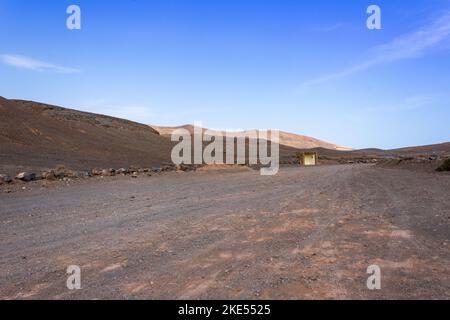 Einsame Wüstenstraße durch eine dürre Landschaft windet sich am Horizont in Richtung vulkanischer Berge, nahe Playa Mujeres und der Papagayo-Küste, Lanzarote, Ca Stockfoto