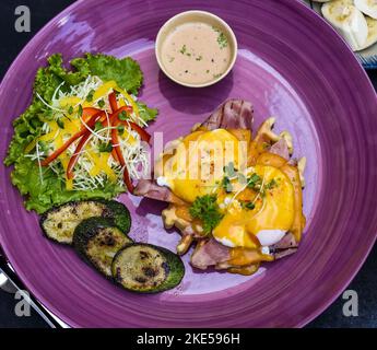 Eier Benedikt (pochierte Eier) auf gegrilltem Schinken mit holland-Sauce auf belgischen Waffeln mit gegrillten Zucchini mit Bananenplatte und einer Tasse Passionssaft Stockfoto