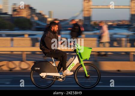 Ein Mann pendelt während der Hauptverkehrszeit mit einem Lime-Elektrofahrrad über die London Bridge. London Bridge, London, Großbritannien. 28 Okt 2022 Stockfoto