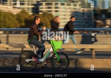 Ein Mann pendelt während der Hauptverkehrszeit mit einem Lime-Elektrofahrrad über die London Bridge. London Bridge, London, Großbritannien. 28 Okt 2022 Stockfoto