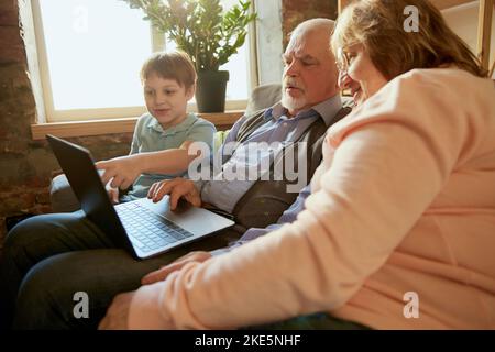 Lebensporträt einer freundlichen Familie, Großelterns und ihres Enkels, die auf dem Sofa sitzen und Zeit miteinander verbringen, mit modernen Gadgets, reden, studieren Stockfoto