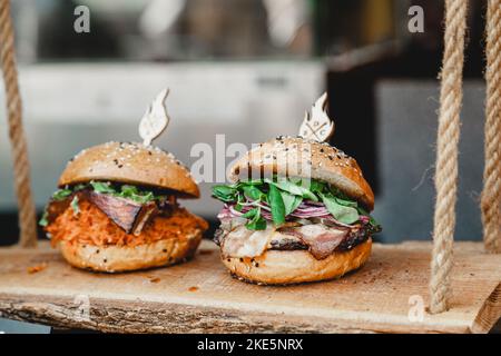 Leckere Burger auf Holzbasis. Zwei leckere hausgemachte Burger mit Rindfleisch, Käse und Gemüse auf einem alten Holztisch. Fett ungesunde Lebensmittel Nahaufnahme Stockfoto