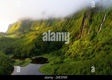 Luftaufnahme eines Cascata da Ribeira do Ferreiro Wasserfalls, der bei Sonnenuntergang auf einer Insel Flores, Azoren, Portugal, beleuchtet wird Stockfoto