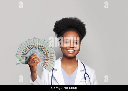 Schöne glückliche afroamerikanische Ärztin lächelt und hält Fan von Geld hundert Dollar Stockfoto