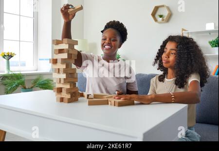 Lachende afroamerikanische Psychologin, die auf der Therapiestunde mit einem Teenager-Mädchen einen stürmenden Turm spielt. Stockfoto