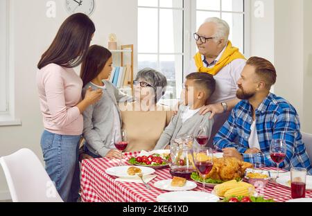 Die große Familie gratuliert Oma, sie umarmen sich beim Familienessen am Tisch im Wohnzimmer. Stockfoto