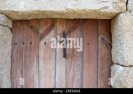 Eine Nahaufnahme einer alten Holztür mit einem metallischen Kreuz darauf Stockfoto