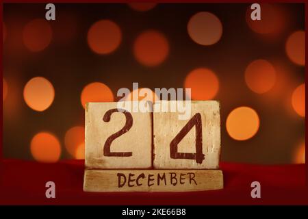 Dezember 24 Weihnachten Abend vintage Holzblock Kalender auf rotem Stoff, festliche Bokeh Lichter Hintergrund Grußkarte Feier Feiertage, Geburtstag, s Stockfoto