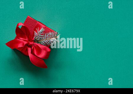 Festliche rote Geschenkbox mit immergrünen Tannenzweigen auf grünem (smaragdgrünen) Hintergrund. Weihnachts- und Neujahrskonzept, Feiertage, Kopierraum. Stockfoto