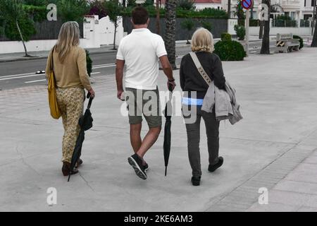 Zwei Frauen und ein Mann mit dem Rücken gedreht und nicht erkennbar auf einer Promenade mit ihren Schirmen geschlossen wegen der Drohung des Regens ruhig gehen Stockfoto