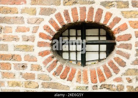 Kleines rundes Fenster mit gusseisernem Zaun in alter Ziegelmauer, Utrecht, Niederlande Stockfoto