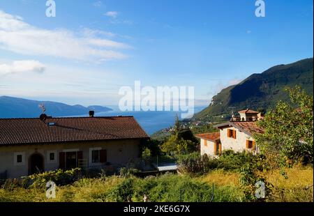 Sonnendurchflutete mediterrane Landschaft mit einem italienischen Dorf mit Blick auf den riesigen blauen Gardasee und die italienischen Alpen in der Nähe von Tignale, Lombardei, Italien Stockfoto