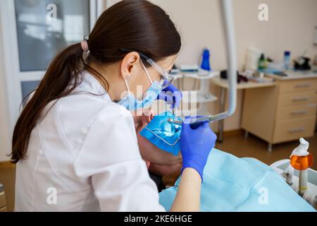 Ein Zahnarzt behandelt einen männlichen Patienten mit zahnmedizinischen Instrumenten. Der Zahnarzt untersucht die Zähne der Patienten in der Zahnklinik. Selektiver Fokus Stockfoto