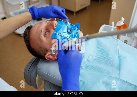 Ein Zahnarzt behandelt einen männlichen Patienten mit zahnmedizinischen Instrumenten. Der Zahnarzt untersucht die Zähne der Patienten in der Zahnklinik. Selektiver Fokus Stockfoto