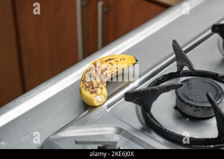 Reife Banane neben dem Gasherd, in einer Küche mit Holzschränken Stockfoto