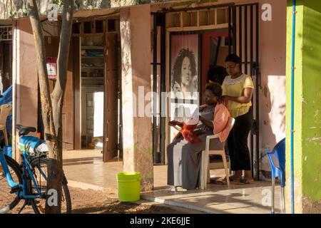 Mtowambu, Tansania - 12.. Oktober 2022: Eine Friseurin und ihre Kundin auf der sonnigen Straße in der kleinen Stadt Mtowambu, Tansania. Stockfoto