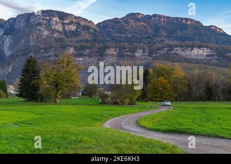 Sonnenuntergang im Rheintal, mit Wiesen und Felder, Bäumen und Bergen im Hintergrund. Föhn mit Wolken und blau, gelb, orange und rotem Himmel Stockfoto