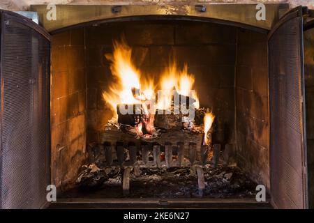 Beleuchteter Holzkamin im Wohnzimmer im alten, renovierten Haus im kanadischen Cottage-Stil aus dem Jahr 1840. Stockfoto