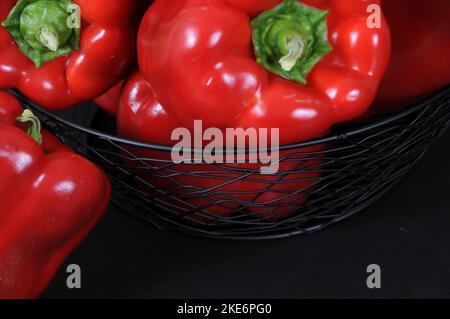 Red Bell Peppers in und um Black Wire Basket Stockfoto