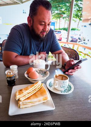 Traditionelles asiatisches Frühstück mit halbgekochten Eiern, Toastbrot mit Butter und Kaya und Kaffee. Chinesischer Stil. Stockfoto