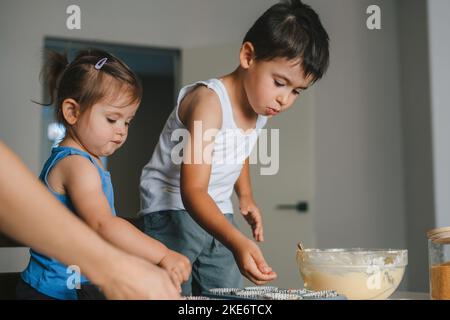 Glückliche Kinder backen Schokolade Muffins in der heimischen Küche, drinnen. Lustige schöne gesunde Kind Spaß mit helfen. Frohe Familie. Glücklich lächeln Stockfoto