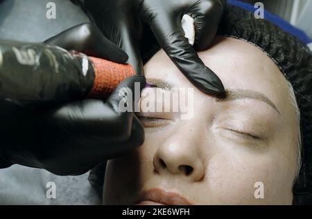 Eine spezielle Nadel Tattoo Maschine macht eine permanente Make-up Korrektur der Augenbrauen einer Frau. Microblading, Pulverbeschichtung Nahaufnahme. Stockfoto