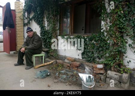 Non Exclusive: MYKOLAYIV, UKRAINE - 09. NOVEMBER 2022 - Ein Mann sitzt neben einem Haus mit Fenstern, die durch Artilleriebeschuss durch russische t Stockfoto