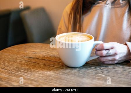 Frau Hände halten Cappuccino Kaffeetassen auf rustikalen Holztisch Hintergrund Stockfoto