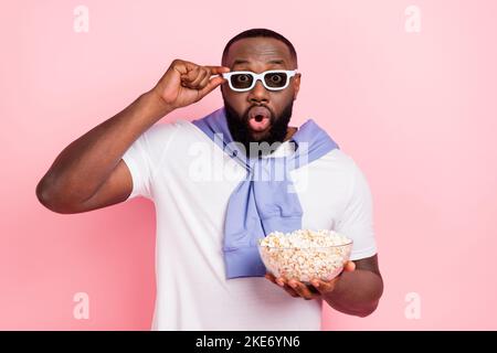 Foto von jungen beeindruckt Kerl sehen Horrorfilm in 3D Theater essen Snack isoliert auf rosa Hintergrund Stockfoto