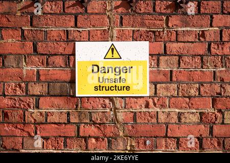 Warnschild für gefährliche Gebäude, das an der roten Ziegelwand angebracht ist Stockfoto