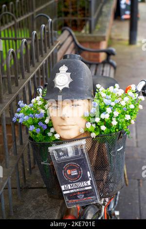 Dummy-Kopf trägt einen Polizist Helm in einem Korb auf einem Fahrrad mit Blumen Werbung für ein lokales Unternehmen Stockfoto