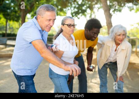 Eine Gruppe von multirassischen erwachsenen Menschen, die im Freien in einem Park patanque spielen Stockfoto