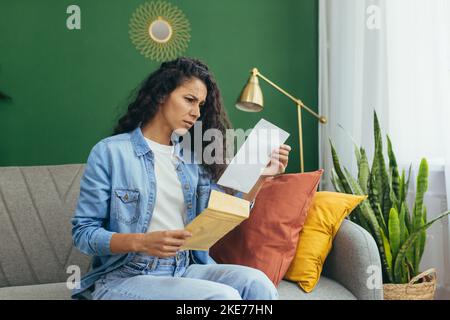 Junge schöne hispanische Frau zu Hause enttäuscht und traurig erhielt Brief von der Universität über schlechte Prüfungsergebnisse, Student mit lockigen Haaren sitzt auf dem Sofa im Wohnzimmer. Stockfoto