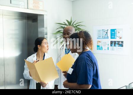 Verschiedene Gruppe von männlichen und weiblichen Ärzten mit Akten, die im Krankenhauskorridor diskutieren Stockfoto