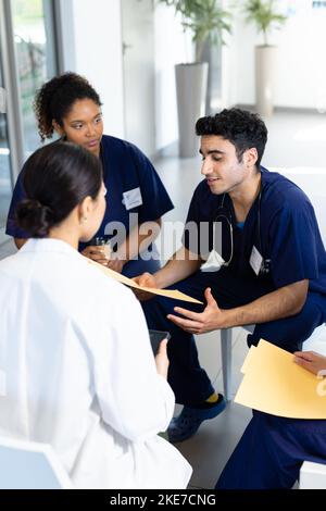 Vertikal einer vielfältigen Gruppe von männlichen und weiblichen Ärzten, die Akten halten, während sie im Krankenhaus diskutiert werden Stockfoto