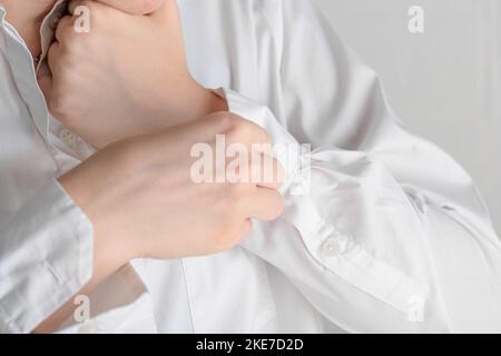 Weibliche Hände befestigen einen Knopf auf dem Ärmel eines weißen Hemdes, Nahaufnahme. Die junge Geschäftsfrau trägt sie für ein Geschäftstreffen und zieht sich morgens an Stockfoto