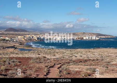 Blick auf die kleine Stadt vom Pfad aus, der vom nahe gelegenen Vulkanberg Montana Roja auftaucht, mit Surfern, die die Wellen auf Teneriffa genießen Stockfoto