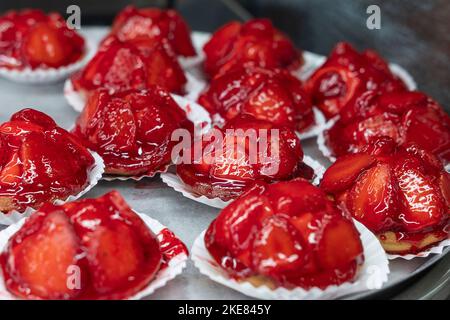 Großes Tablett mit köstlichen Erdbeertörtchen, Minitörtchen gefüllt mit süßem Pudding und gekrönt mit Scheiben saftiger roter Beeren, Gelifiziertem Sirup Stockfoto