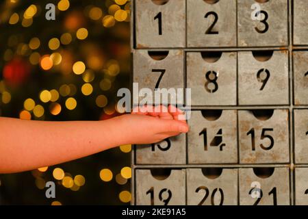 adventskalender im Vintage-Stil und Kinderhände in der Nähe des Weihnachtsbaums mit Spielzeugen, die Girlande auf dem Hintergrund des Zimmers leuchten. Weihnachtstraditionen und -Symbole. Stockfoto