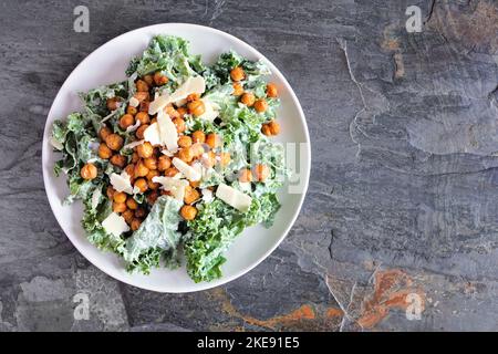 Vegetarischer Caesar-Salat mit Kichererbsen, Grünkohl und Joghurt-Dressing. Draufsicht auf dunklem Schieferhintergrund. Pflanzliches Lebensmittelkonzept. Stockfoto