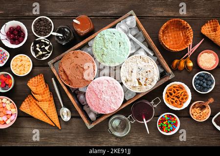 Sommerliches Eisbuffet mit einer Mischung aus Aromen und süßen Belägen. Draufsicht Tischszene auf dunklem Holzhintergrund. Stockfoto